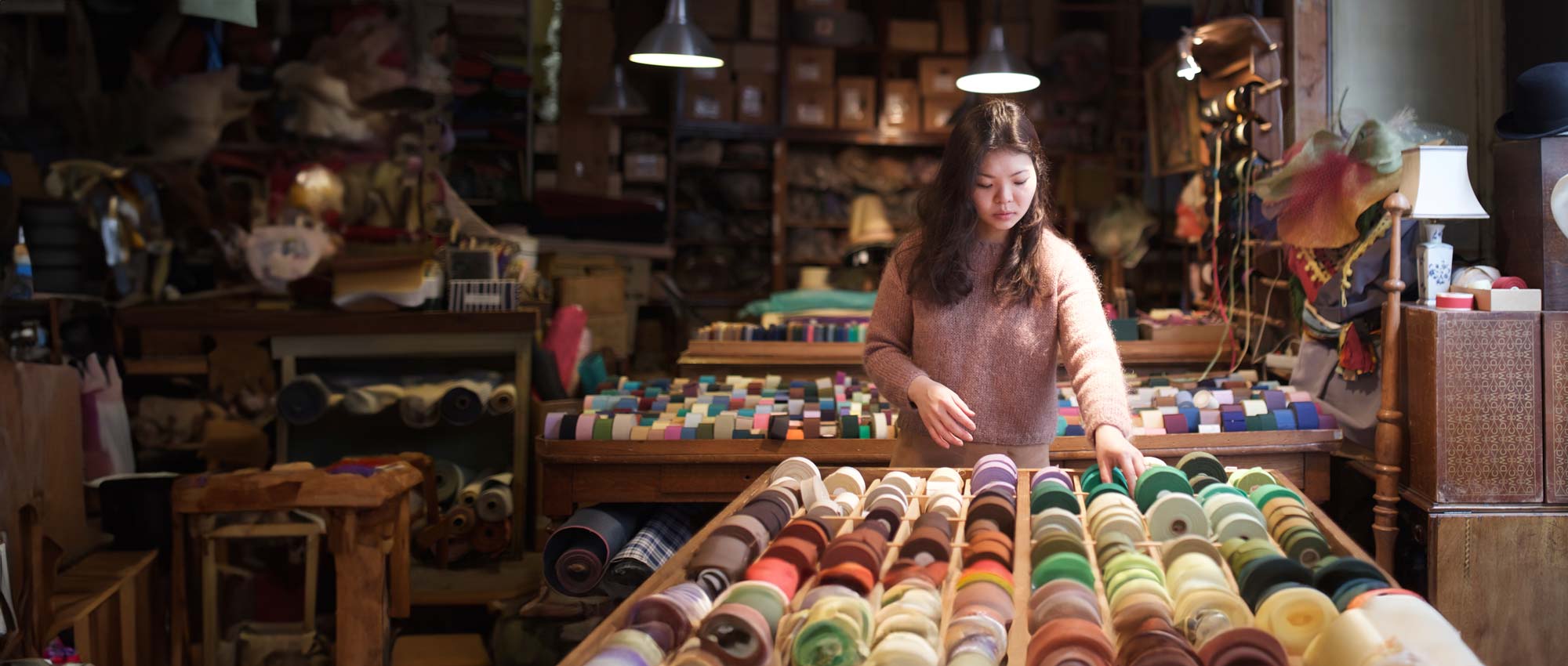 A woman stands looking at a set of fabric spools