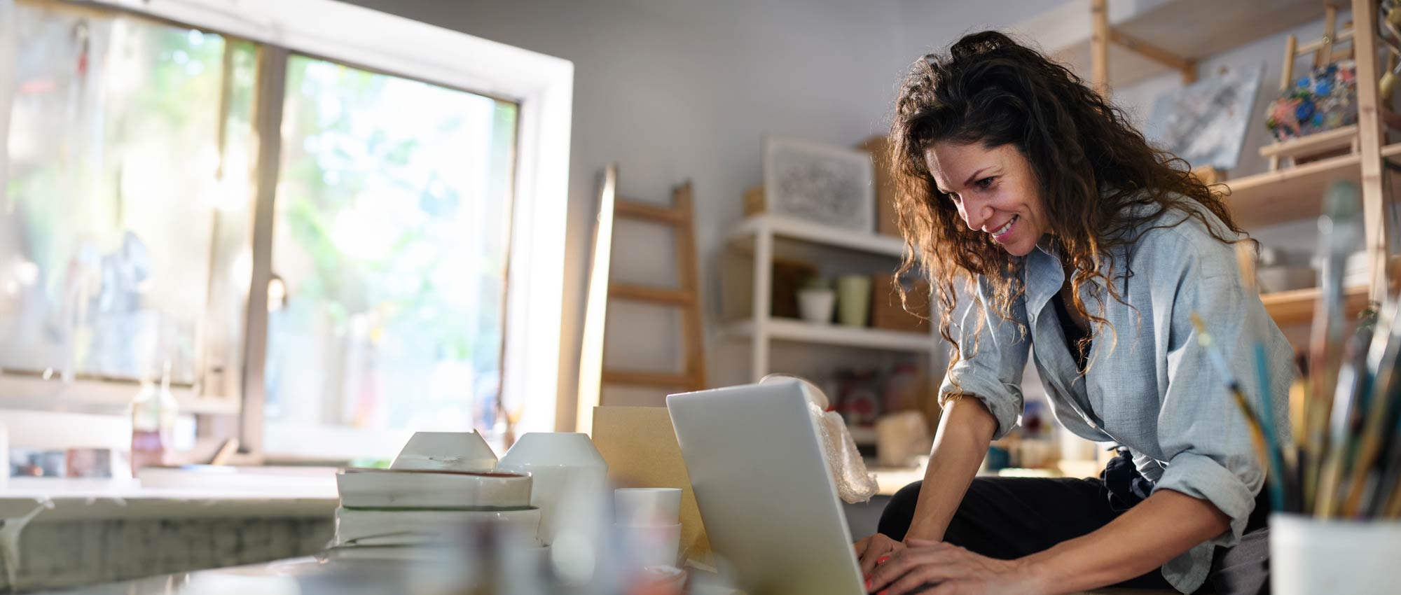 A woman is sitting at a table smiling looking at a laptop computer